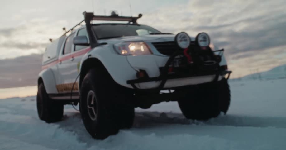A rugged search and rescue super jeep powerfully plows through a deep, snowy landscape at dusk in slow motion