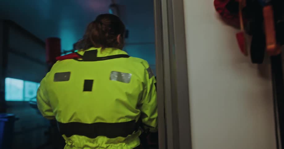 A maritime rescue team in full gear walks with purpose from the locker room to the boat hangar in slow motion