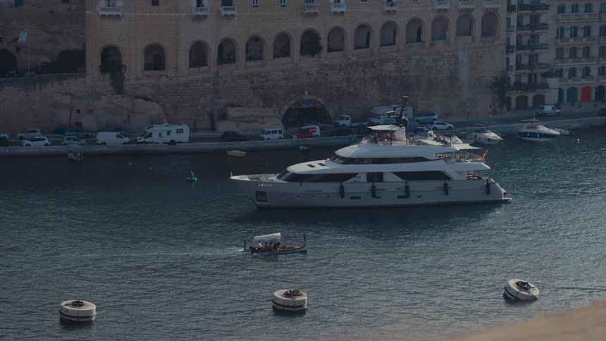 A high-angle view of a luxury yacht and a small tour boat in the Grand Harbour of Valletta, Malta