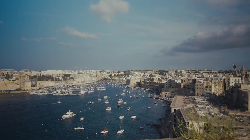 Boats and yachts fill the bay of a sunny Mediterranean coastal city with historic stone buildings