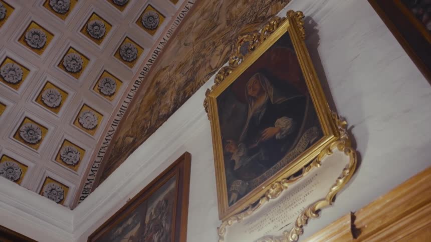 A low-angle shot reveals an ornate gilded portrait and a beautifully detailed coffered ceiling inside a historic European hall