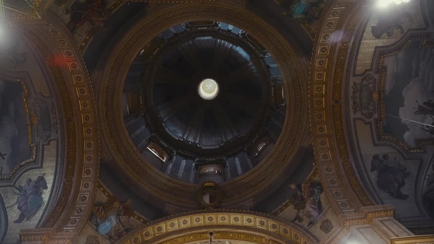 A slow, rotating, low-angle shot looking up at the magnificent and ornate golden dome of a historic European cathedral