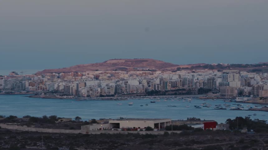 A scenic panning view captures the tranquil coastal city of St. Paul's Bay in Malta as twilight settles over the harbor