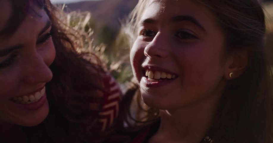 A mother comforts her pouting daughter, making her smile in a warm, sunlit, slow-motion close-up