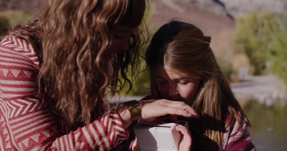A mother patiently shows her daughter how to load film into a retro instant camera as they enjoy a day outdoors together