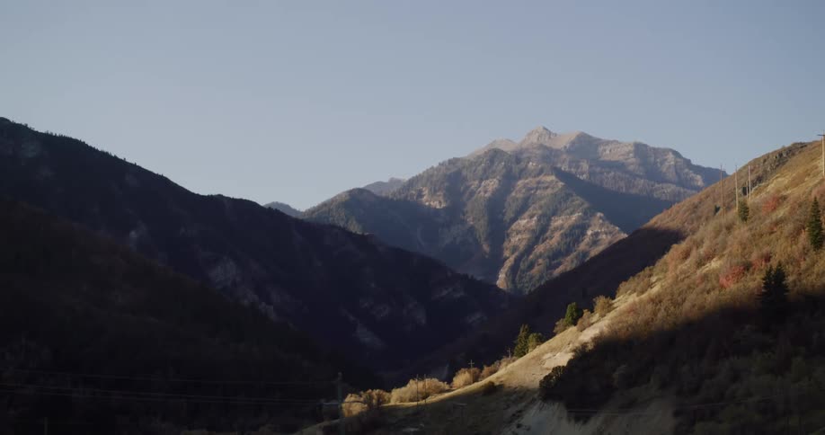 Slowly tilting down from a sunlit mountain peak to reveal a beautiful valley and a winding road below