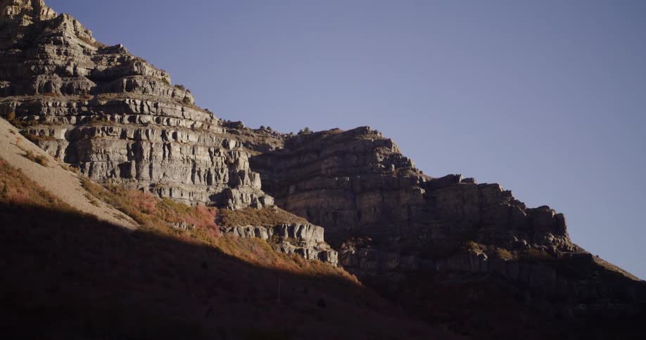 A timelapse of the sun rising and casting light on a rugged, rocky mountain face during autumn