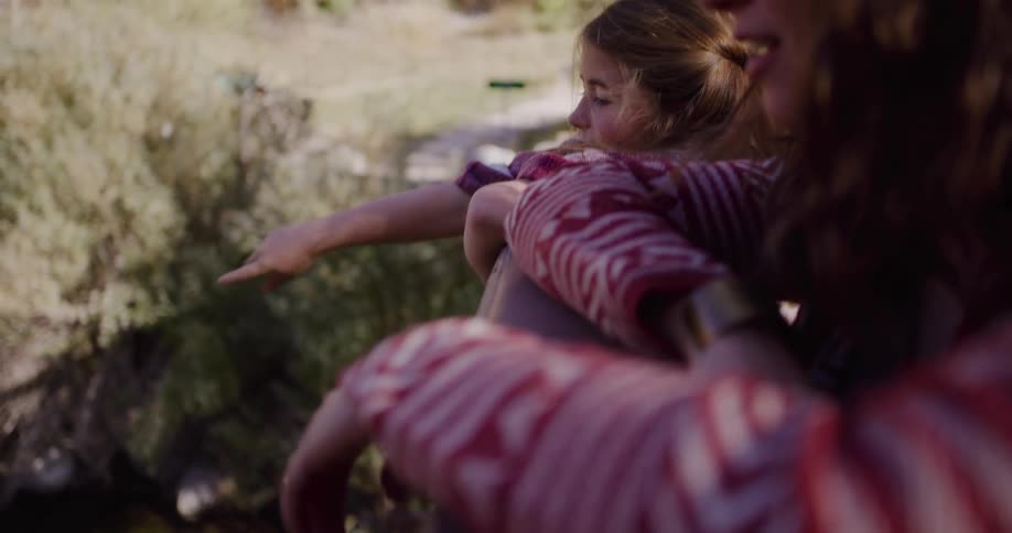 A young girl points something out to her mother as they sit together enjoying a quiet moment in nature