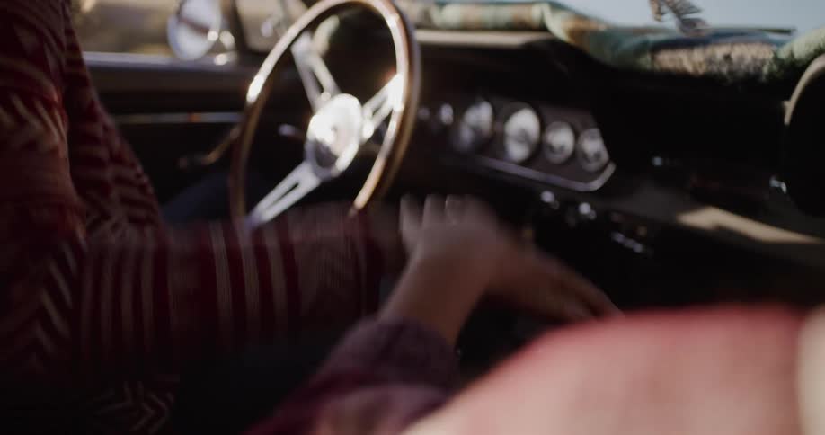 Carefree driver and passenger enjoy a road trip, dancing and grooving to the music in their classic convertible