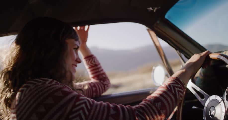 A carefree woman smiles while driving a vintage car on a sun-drenched road trip, feeling the breeze from the open window