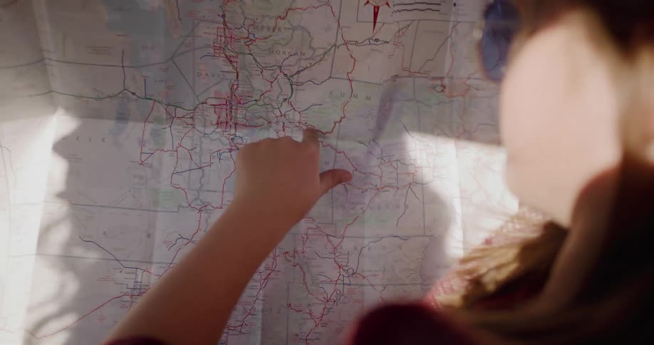 A young woman traces her journey on a physical map of Utah while planning her sunny road trip