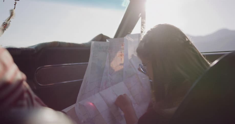 Sunlight streams into a vintage car as a young woman with braided hair studies a road map for her next adventure