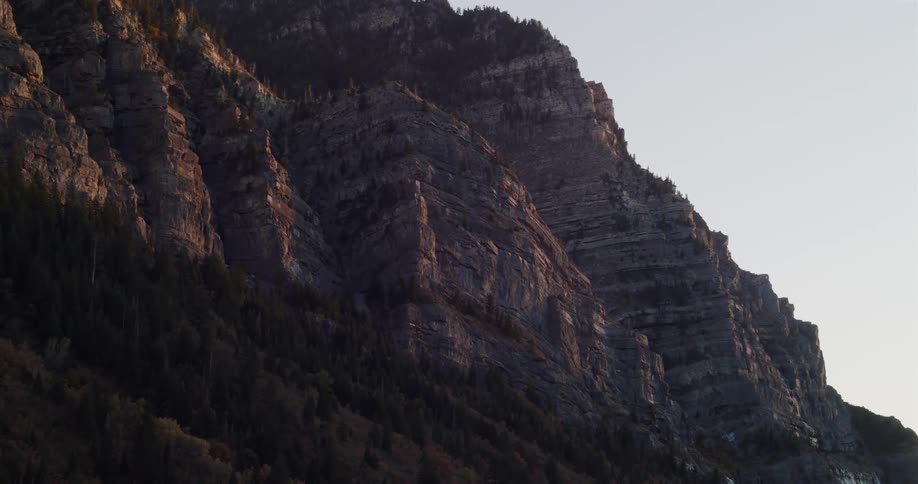 A static shot captures the warm light of sunrise hitting a rugged, rocky mountain cliff