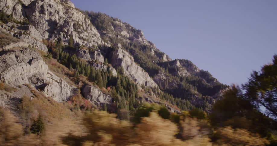 A scenic drive past a majestic rocky mountain range adorned with vibrant autumn foliage on a clear day