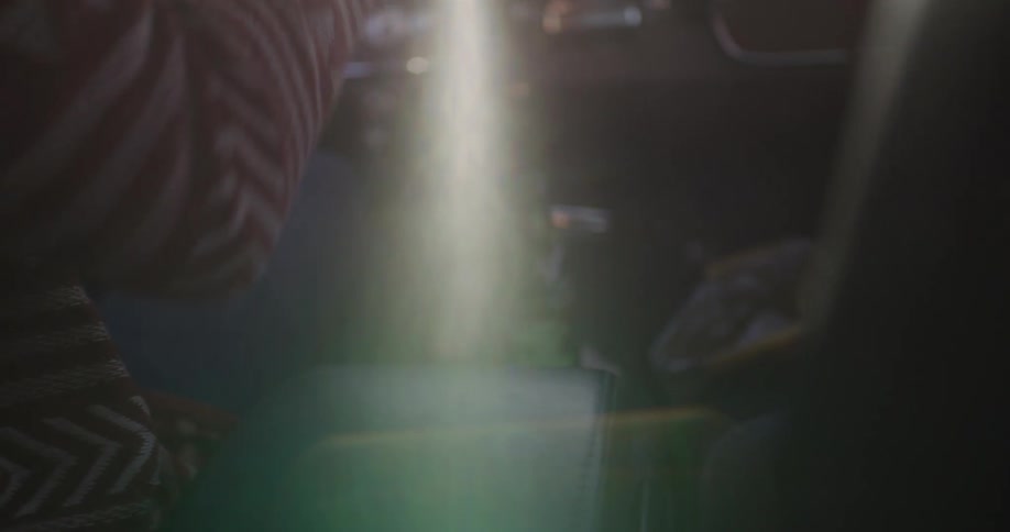 A person reaches for a green soda bottle from the console of a classic car as a warm sun flare streams through the window