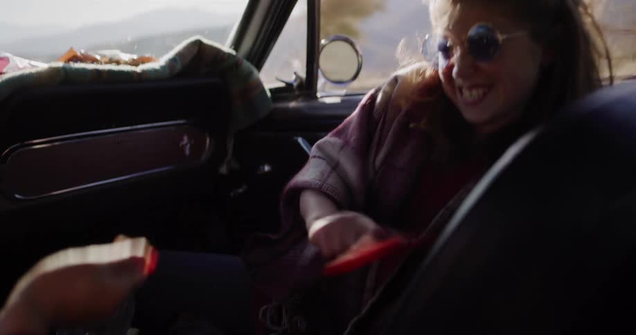 Playful young friends laugh and tease each other with candy during a sun-drenched road trip in their classic convertible