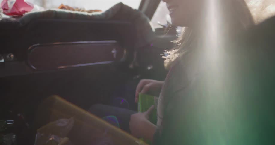 A carefree girl with sunglasses laughs and smiles as the wind blows through her hair during a sunny road trip in a vintage convertible