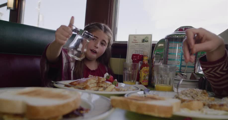 A happy young girl playfully pours syrup all over her pancakes and then drinks the rest in a classic American diner
