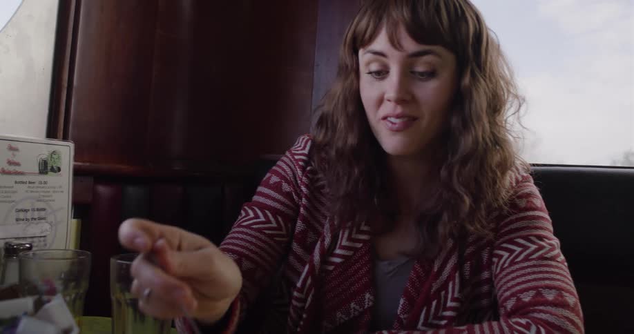 A young woman in a cozy sweater enjoys a meal and an animated conversation with a companion in a classic diner booth