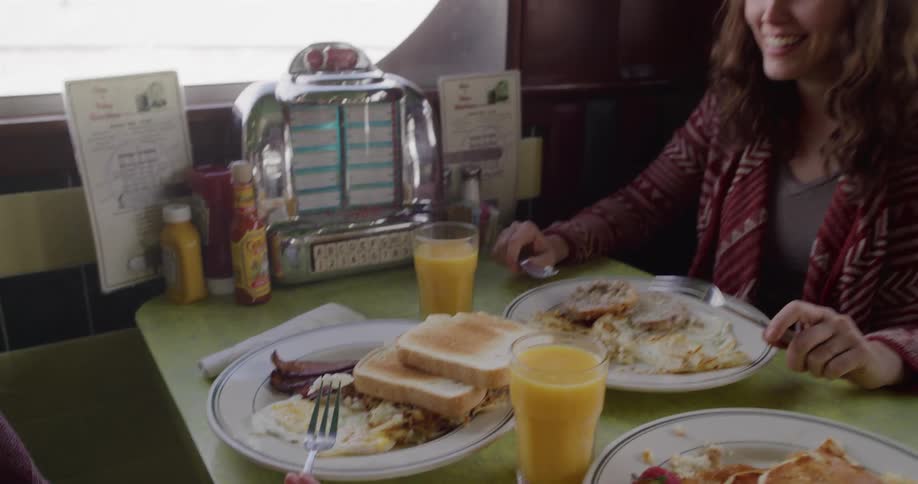 A mother and her daughter laugh and smile while enjoying a classic breakfast together in a retro-style diner booth