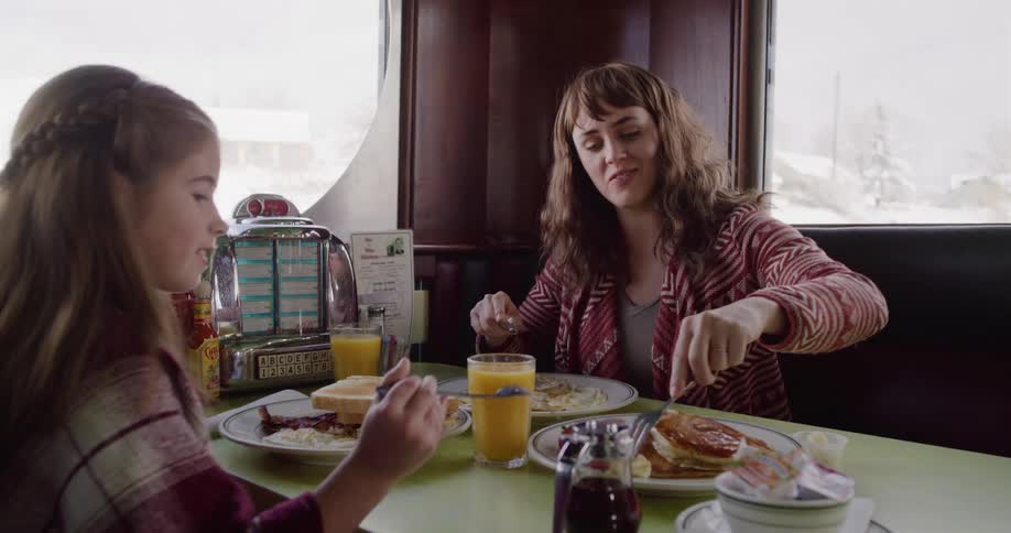 A smiling mother and her daughter enjoy a cozy breakfast together in a classic American diner booth