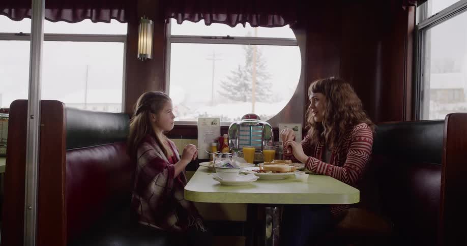 A mother and her young daughter enjoy a warm breakfast together in a cozy retro diner booth on a snowy winter day