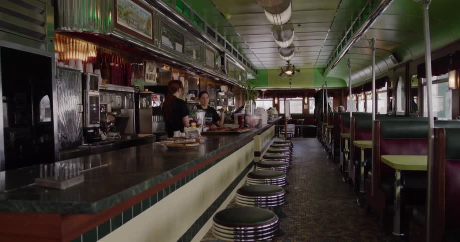Slowly pulling back from two waitresses talking at the counter inside a vintage, empty American-style diner