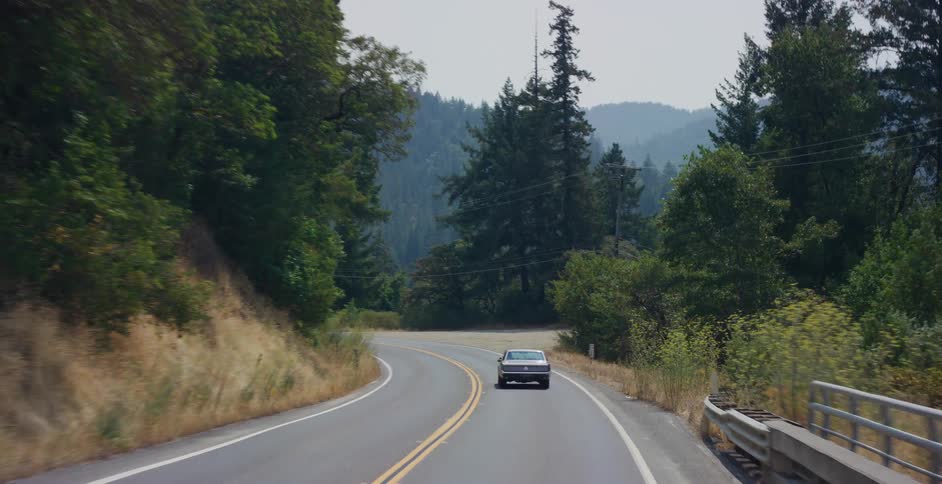 Rear view of a classic car cruising down a winding highway through a remote forest landscape