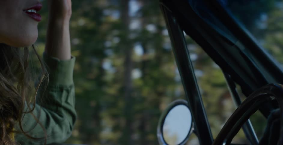 A young woman enjoys a scenic drive through a sun-dappled forest in her classic car