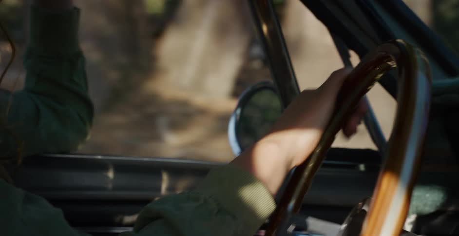 Slow motion close-up of a person's hands on the wooden steering wheel of a classic car driving down a dirt road through the forest