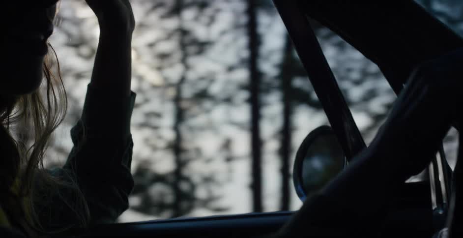 A silhouetted woman enjoys a peaceful drive in her classic car as the sun sets through the forest trees