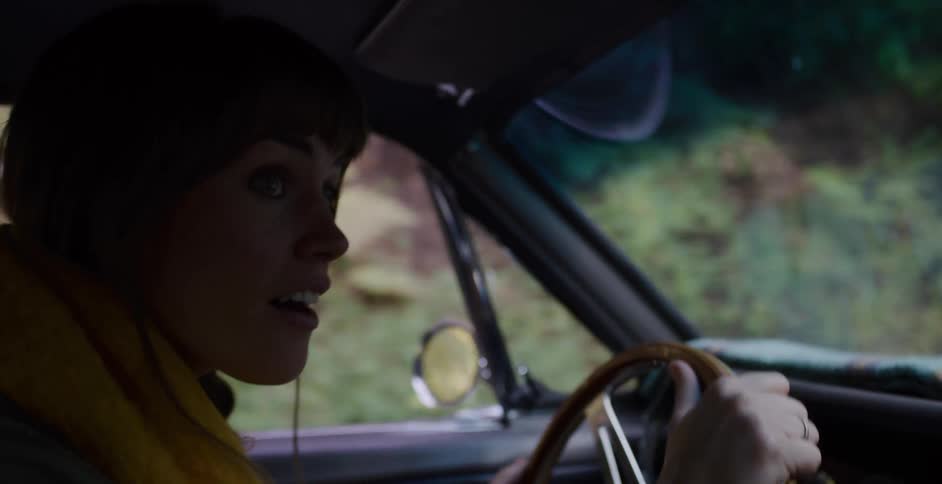 A happy woman in a vintage car drives through a forest, her expression turning to surprise in slow motion