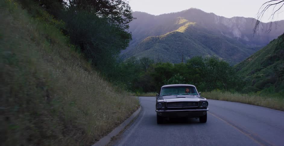 A classic muscle car drives down a beautiful winding mountain road during the golden hour