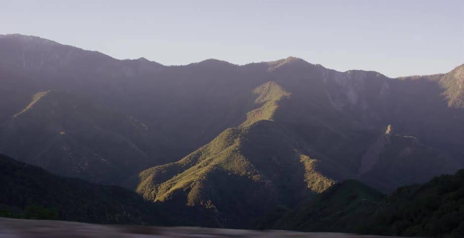 A slow pan from a moving vehicle reveals a vast, sunlit mountain range at sunrise