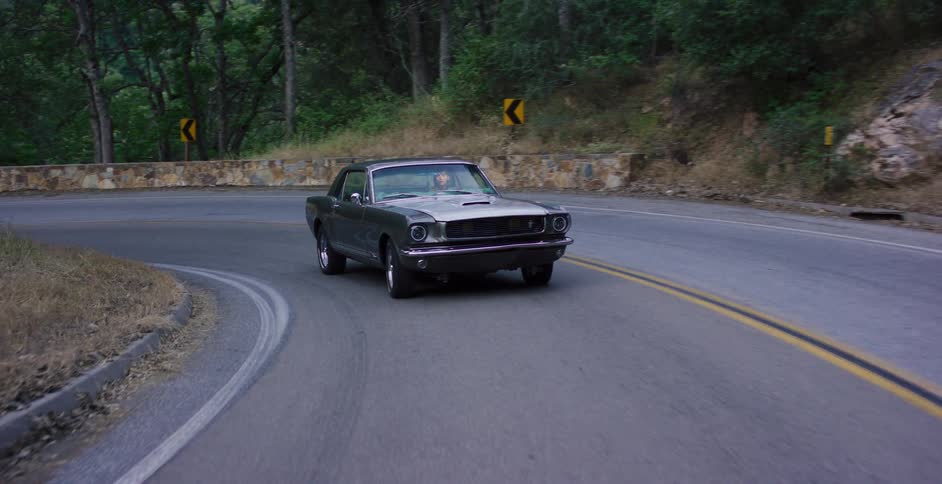 Slow motion shot of a vintage grey Ford Mustang driving around a sharp curve on a wooded road