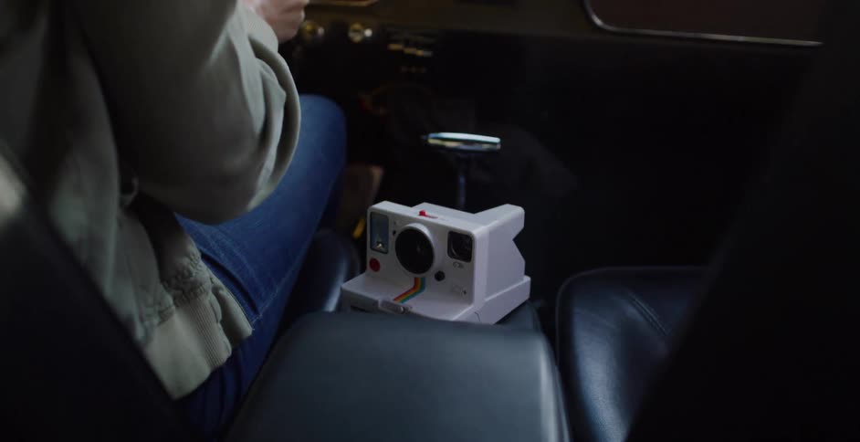 A classic instant camera sits on the center console of a vintage car ready for a road trip