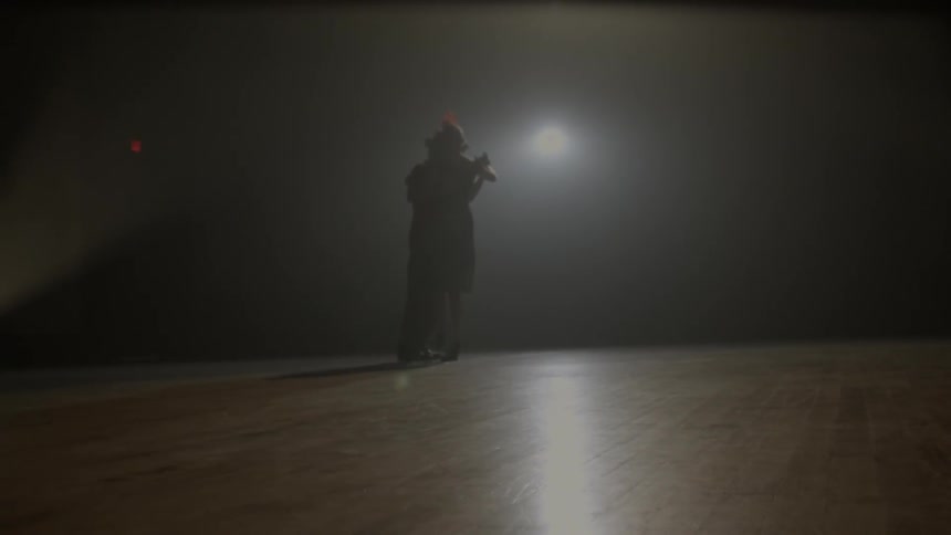 A light shines down on a man and woman dancing on a wood floor