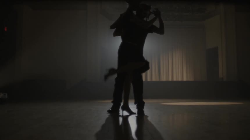 A man and woman dance together on a dark stage