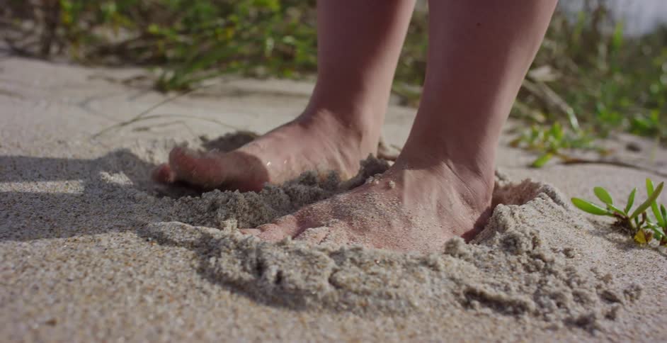 A person enjoys the sensation of wiggling their bare feet in the soft, warm sand of a beach