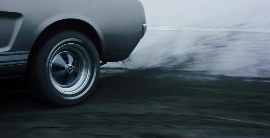 Side view of a classic grey muscle car drifting in slow motion on a wet black sand beach