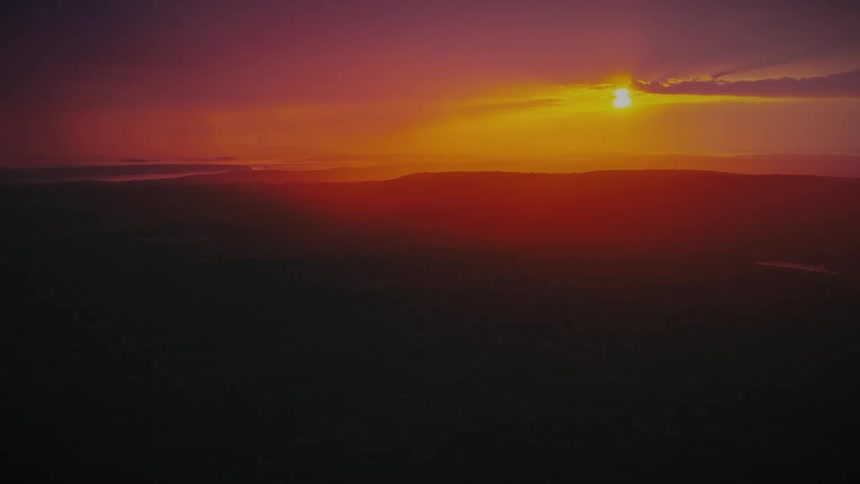 A vibrant purple and orange sunset glows over a vast, silhouetted mountain range at dusk
