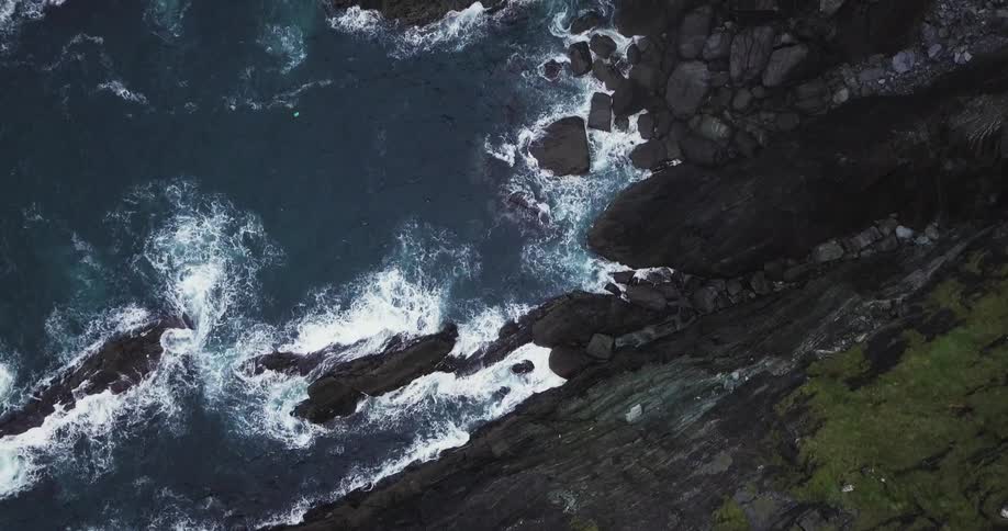 The rough waters splash against the rocks of a cliff