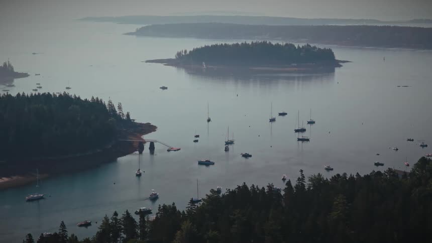 A slow zoom out reveals a vast, serene harbor filled with anchored yachts and sailboats on a hazy day