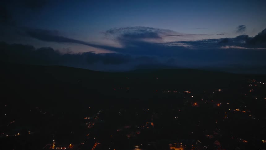 A quiet town settles in for the night, its lights twinkling under a deep blue twilight sky in a still aerial view
