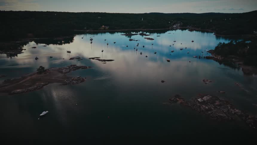 Sailboats rest on the glassy water of a quiet cove at twilight, their reflections perfectly mirrored in the still surface in this beautiful aerial view