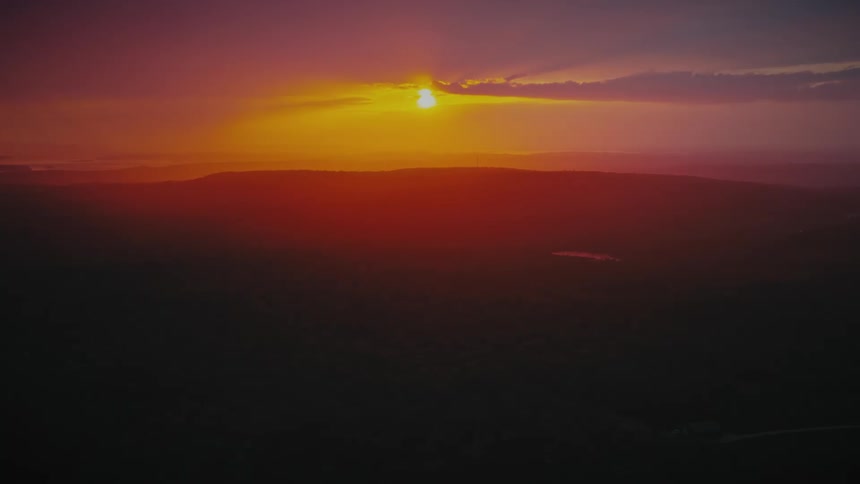 A brilliant orange and red sunset casts its warm glow over a vast, silhouetted mountain range