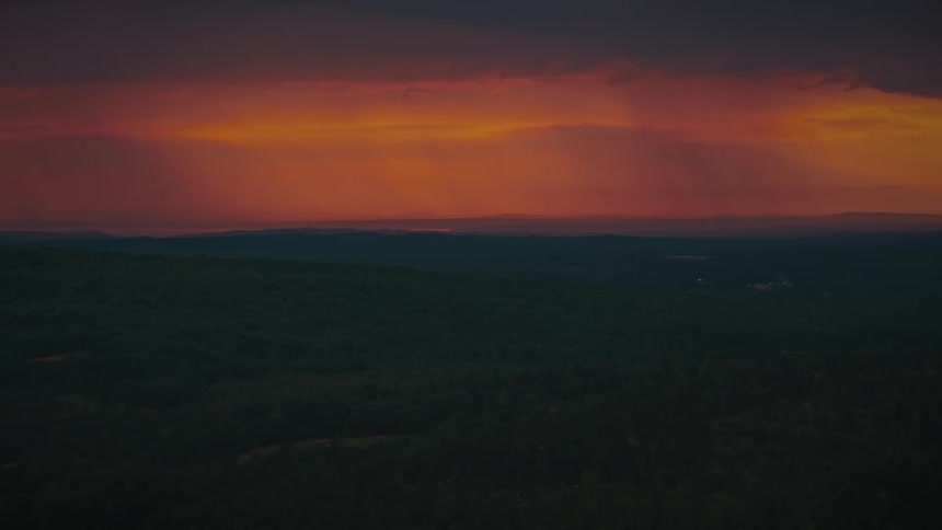A dramatic, fiery orange and red sunset illuminates the sky above a vast, dark forest