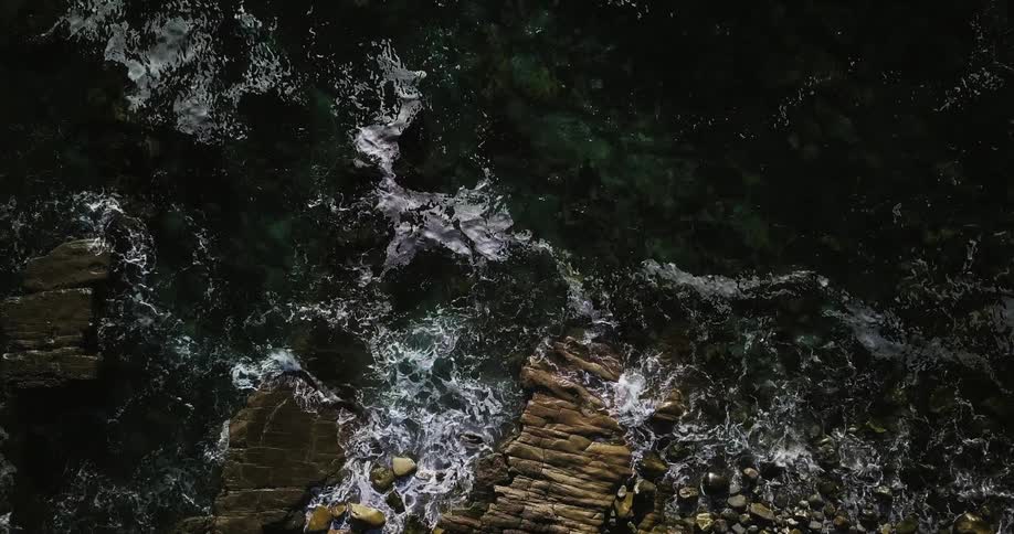 The waves crash against the rocky shore pulling back after