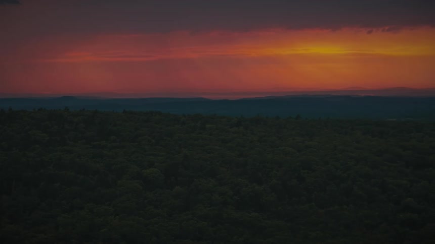A vibrant and dramatic red sunset glows over a silhouetted forest and distant mountains