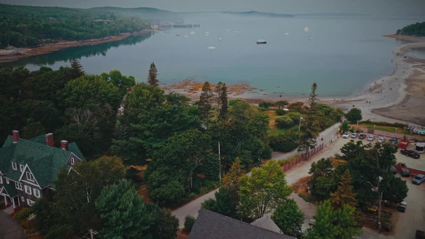 A slow aerial pullback reveals the quaint coastal town of Bar Harbor, Maine, with its harbor, boats, and the iconic land bridge to Bar Island visible at low tide